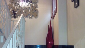 A staircase with a modern chandelier, a decorative wall piece, and a red vase.