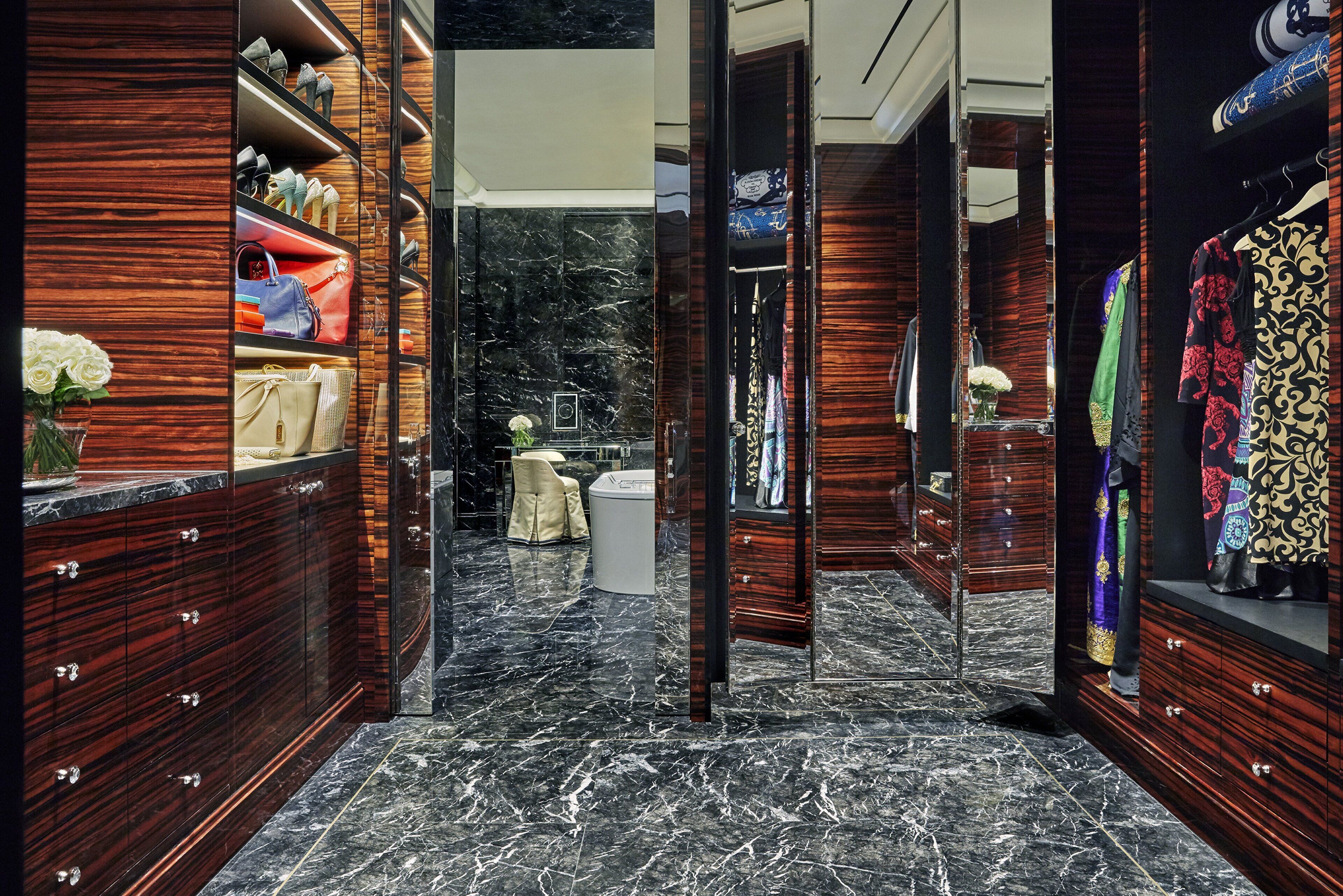 A luxurious walk-in closet with marble flooring and wooden cabinetry, featuring a variety of handbags and clothing.