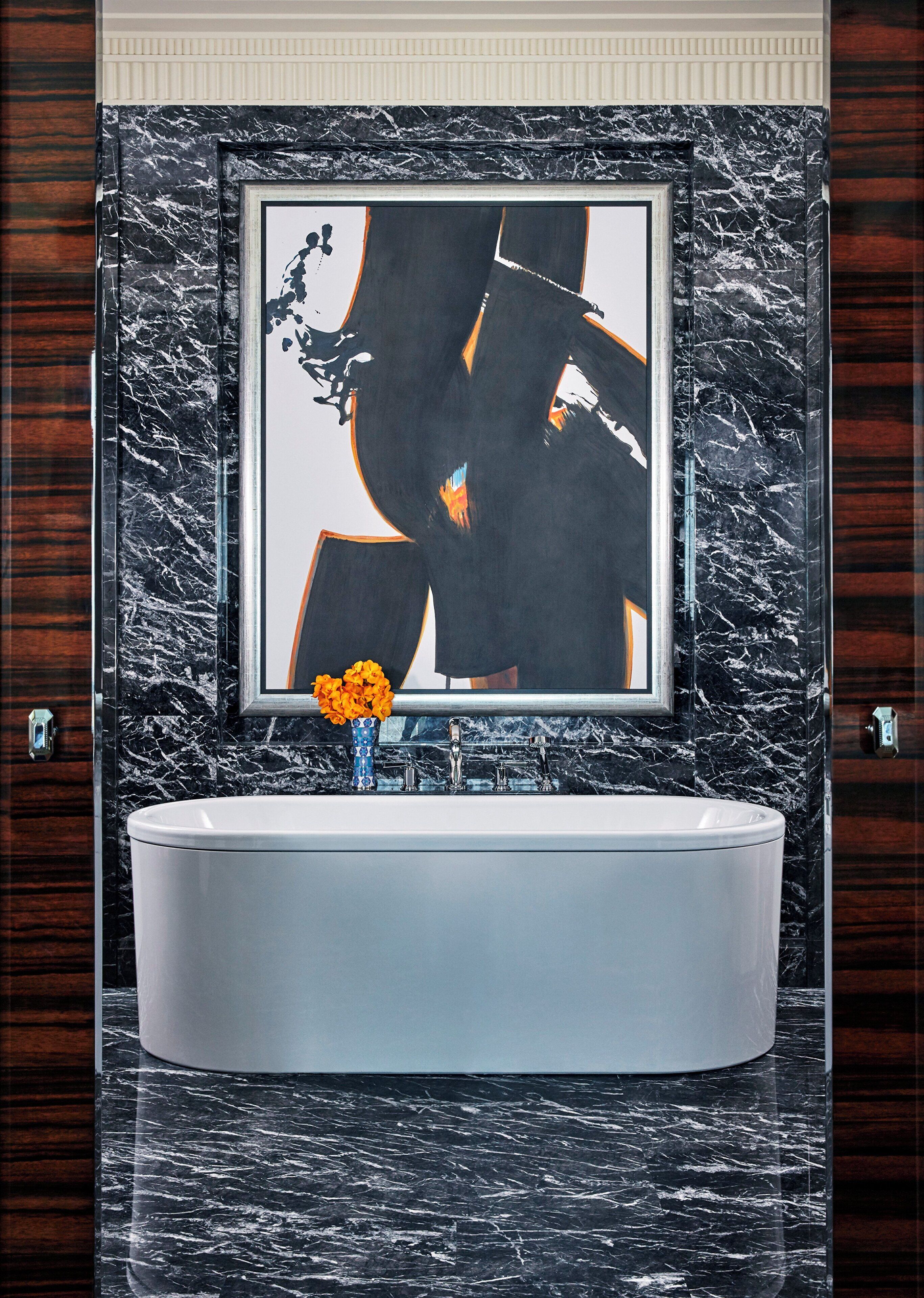 A bathroom with a marble sink, a framed abstract artwork, and a vase with flowers.