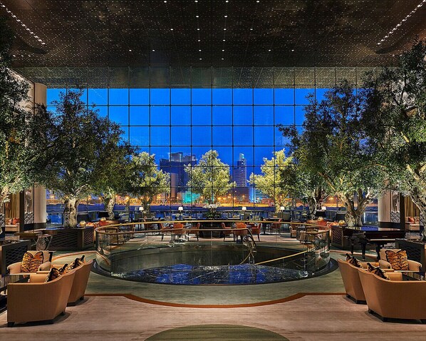 Un vaste espace intérieur agrémenté d’un élément aquatique central, entouré de coins salon et doté de grandes fenêtres offrant une vue sur la ville.