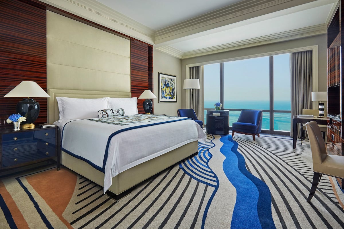 A hotel room with a large bed, a desk, a chair, and a view of the ocean.