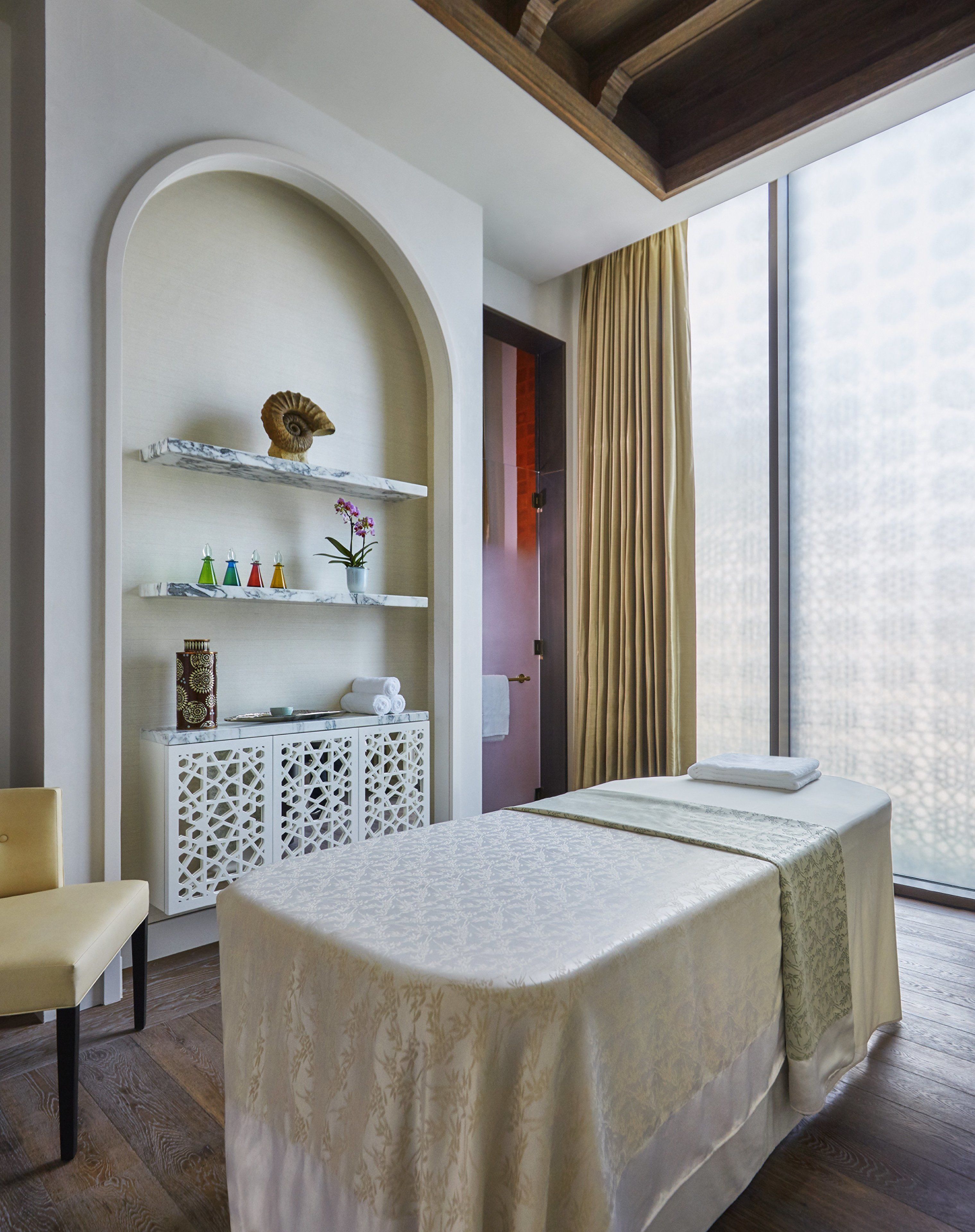 Ein Zimmer mit einem Bett, einer kleinen Sitzecke, einem dekorativen Regal mit Gegenständen und einem großen Fenster mit Vorhängen.