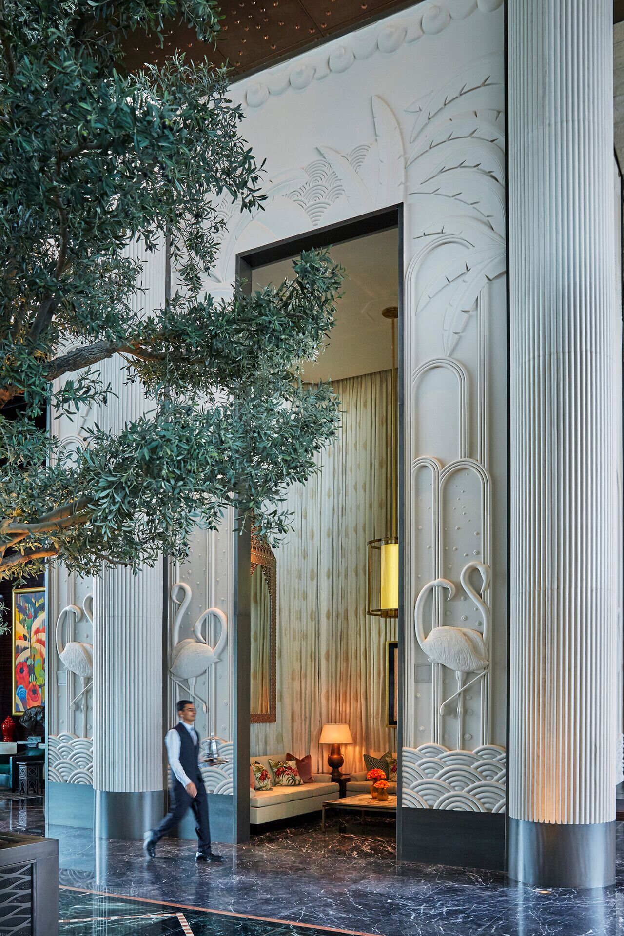 A lobby with marble flooring, a large tree, and a man walking.