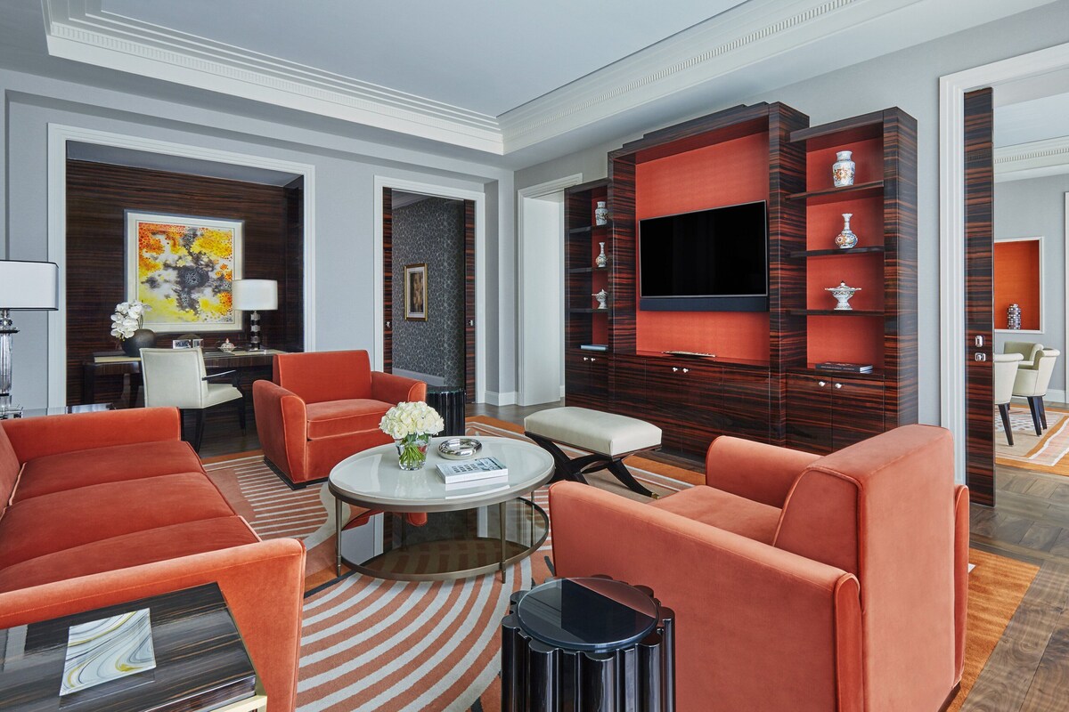A modern living room with orange furniture, a flat-screen TV, and decorative items on shelves.