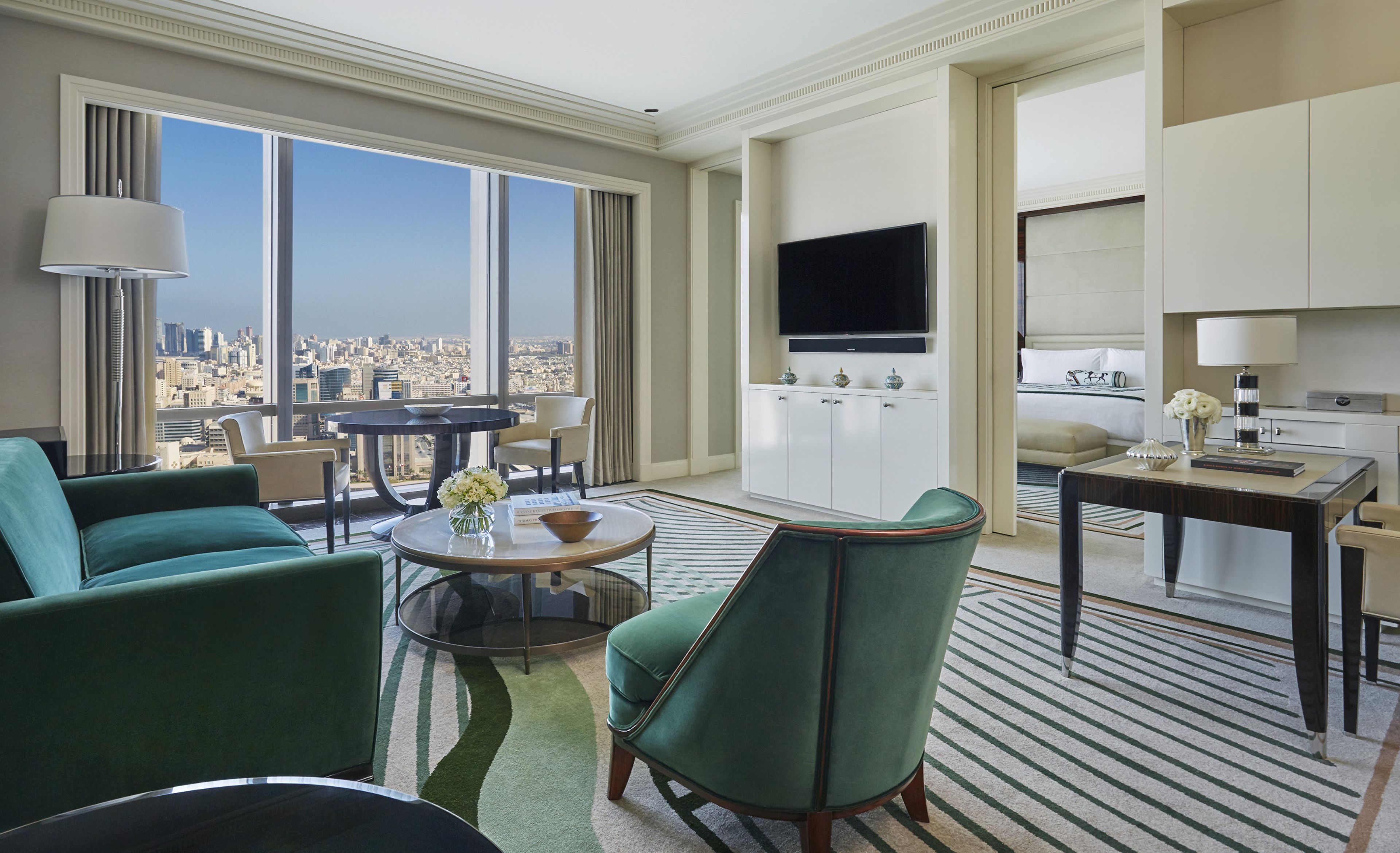 A hotel room with a city view, a dining area, and a living room with green upholstered furniture.
