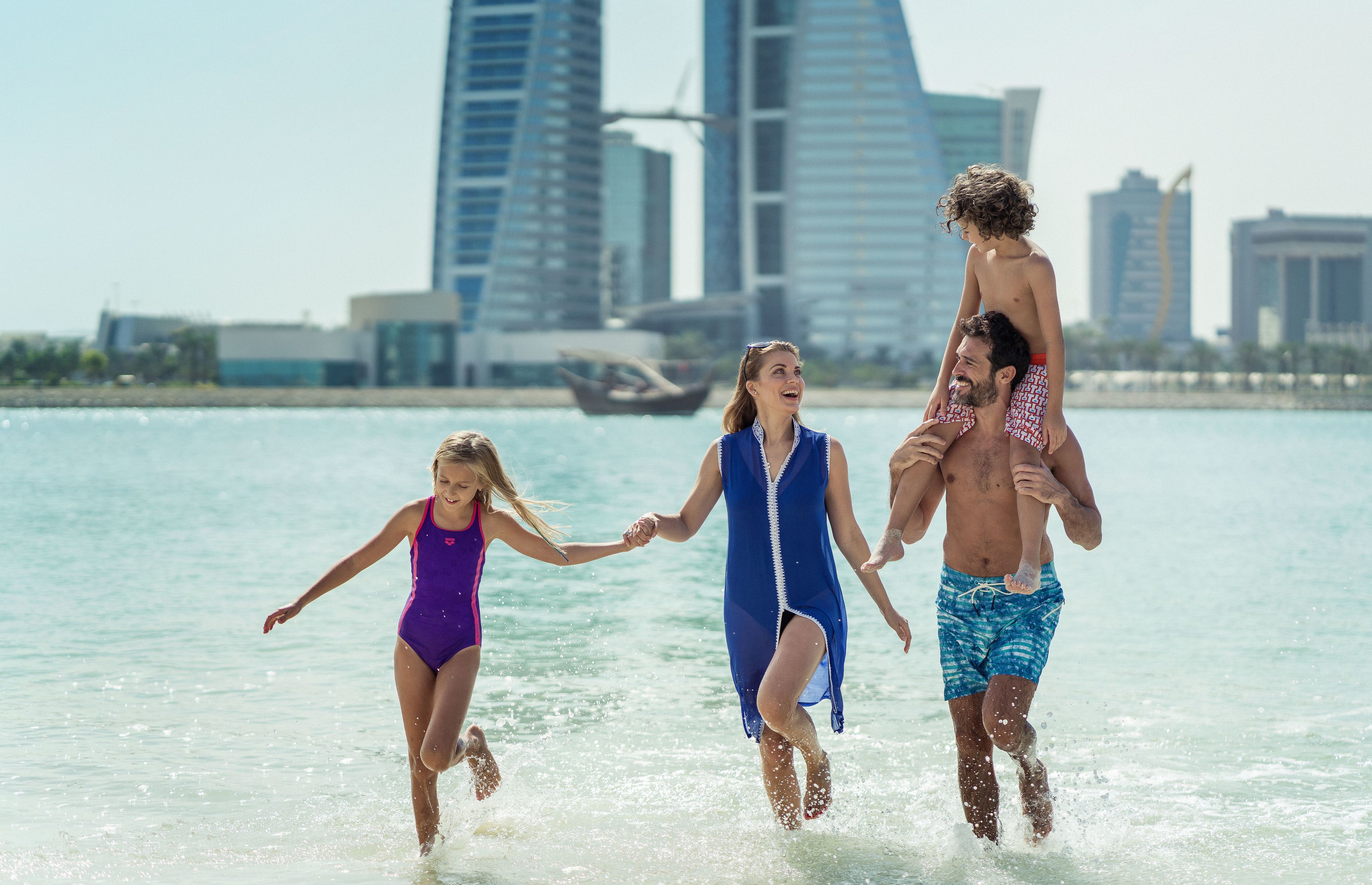 A family running in shallow water with a cityscape in the background.