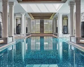 A large indoor swimming pool with clear blue water, surrounded by white columns and a tiled floor. - Four Seasons Hotel Bahrain Bay (Manama)