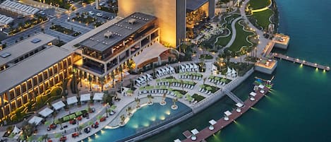 Un hotel frente al agua con piscina, zonas de descanso y un gran edificio con columnas verticales.