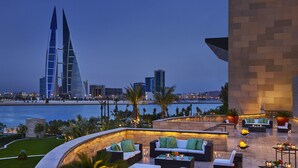 A rooftop lounge with outdoor seating, a view of the water, and modern buildings in the background. - Four Seasons Hotel Bahrain Bay (Manama)