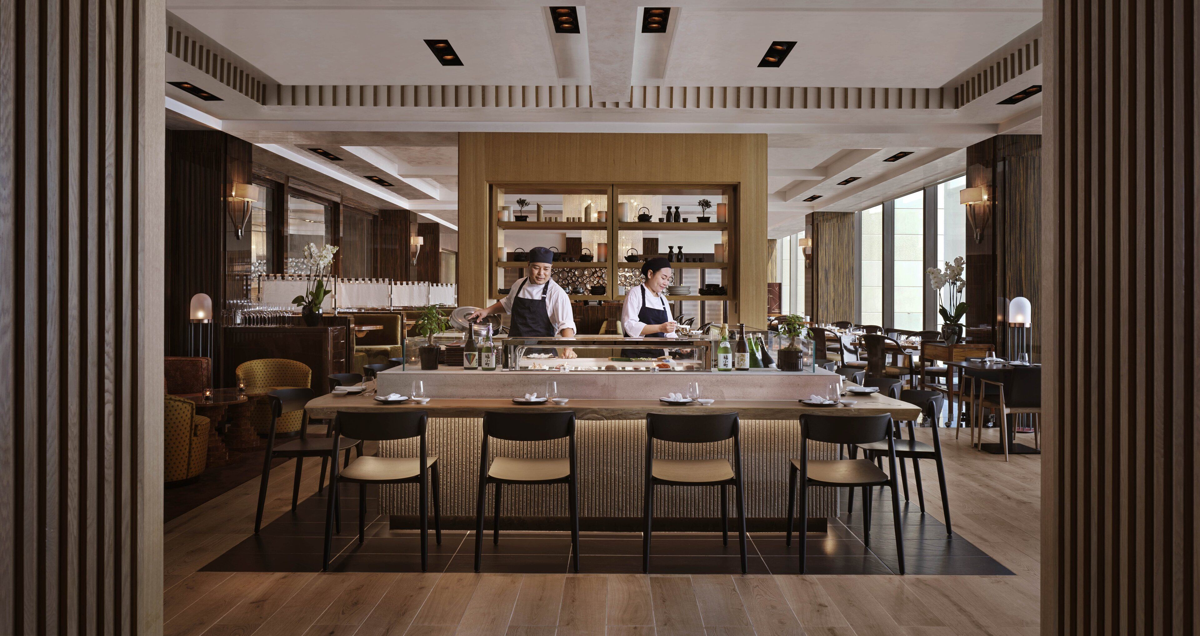 A modern restaurant with a long counter, bar stools, and a bar area.