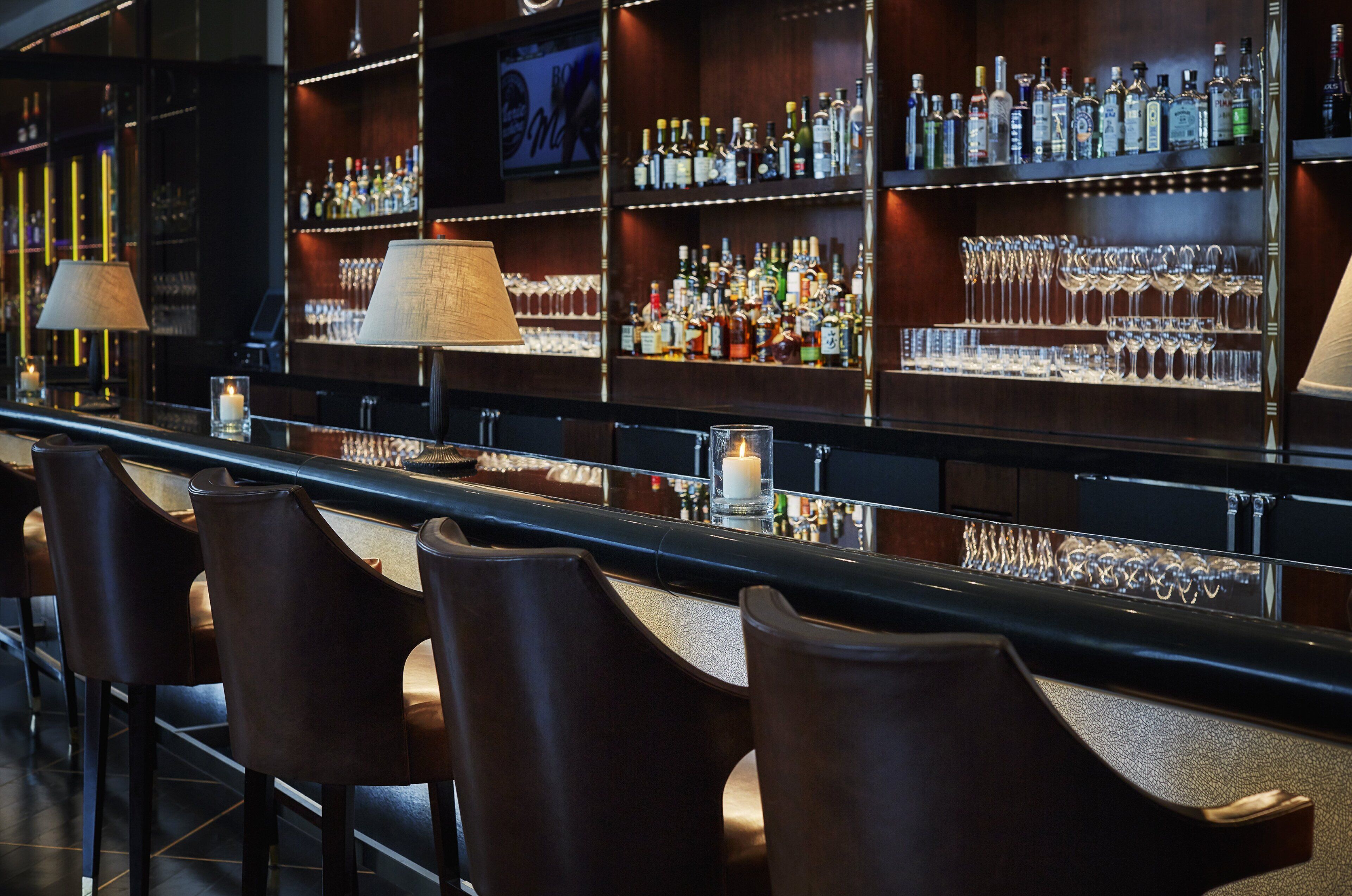 A bar area with multiple shelves of liquor bottles, glasses, and a few bar stools.