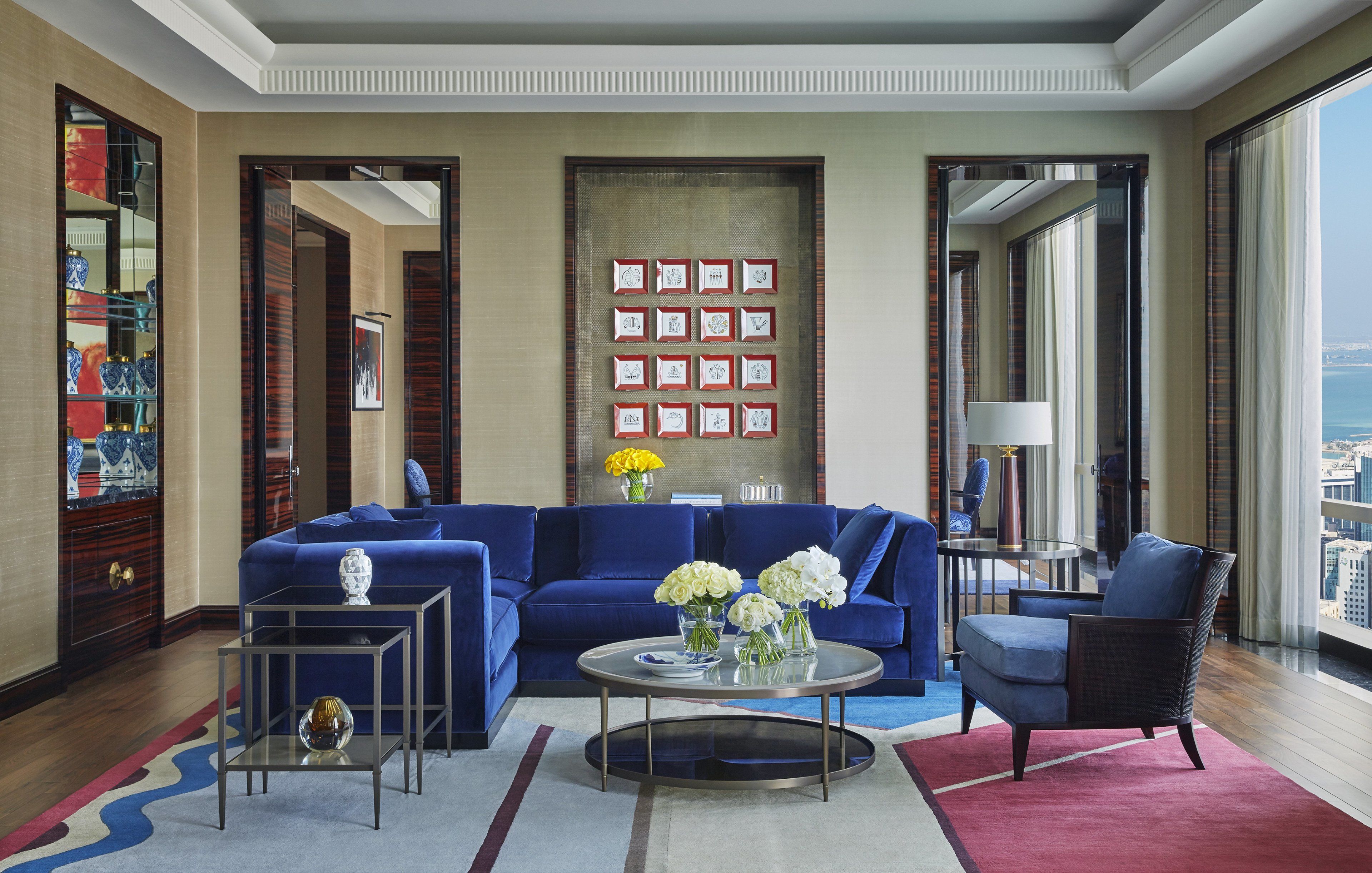 A modern living room with a blue sofa, a coffee table, and a view of the city through large windows.
