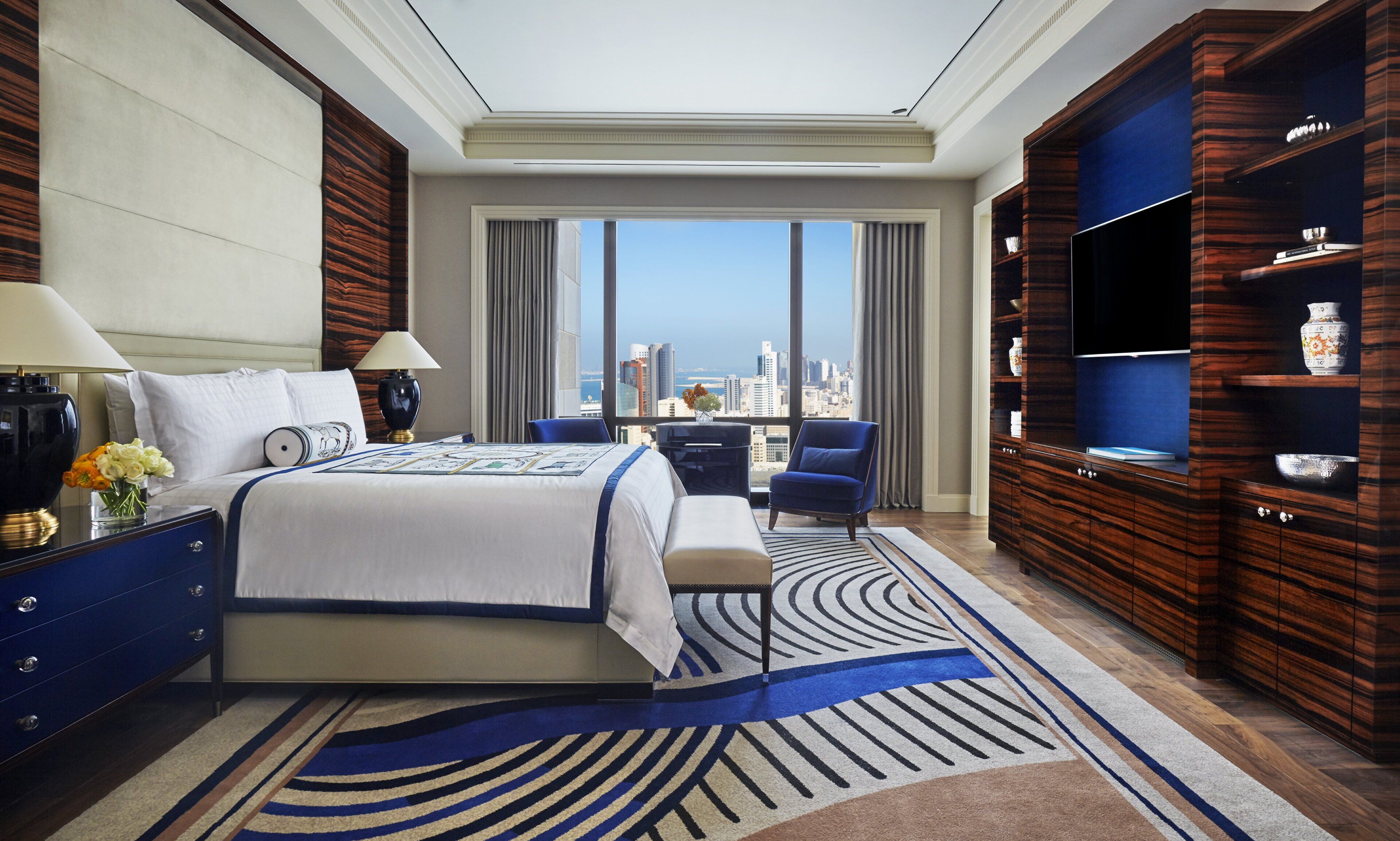 Ein Hotelzimmer mit einem großen Bett, einem Schreibtisch, einem Sessel, einem Fernseher und Blick auf die Stadt.