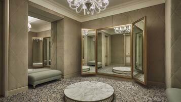 A luxurious bathroom with a large mirror, a round marble table, and a tufted bench.