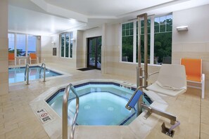 Un espace piscine intérieur moderne, doté de parois en verre transparent, d’un jacuzzi et d’un coin salon avec des fauteuils orange.