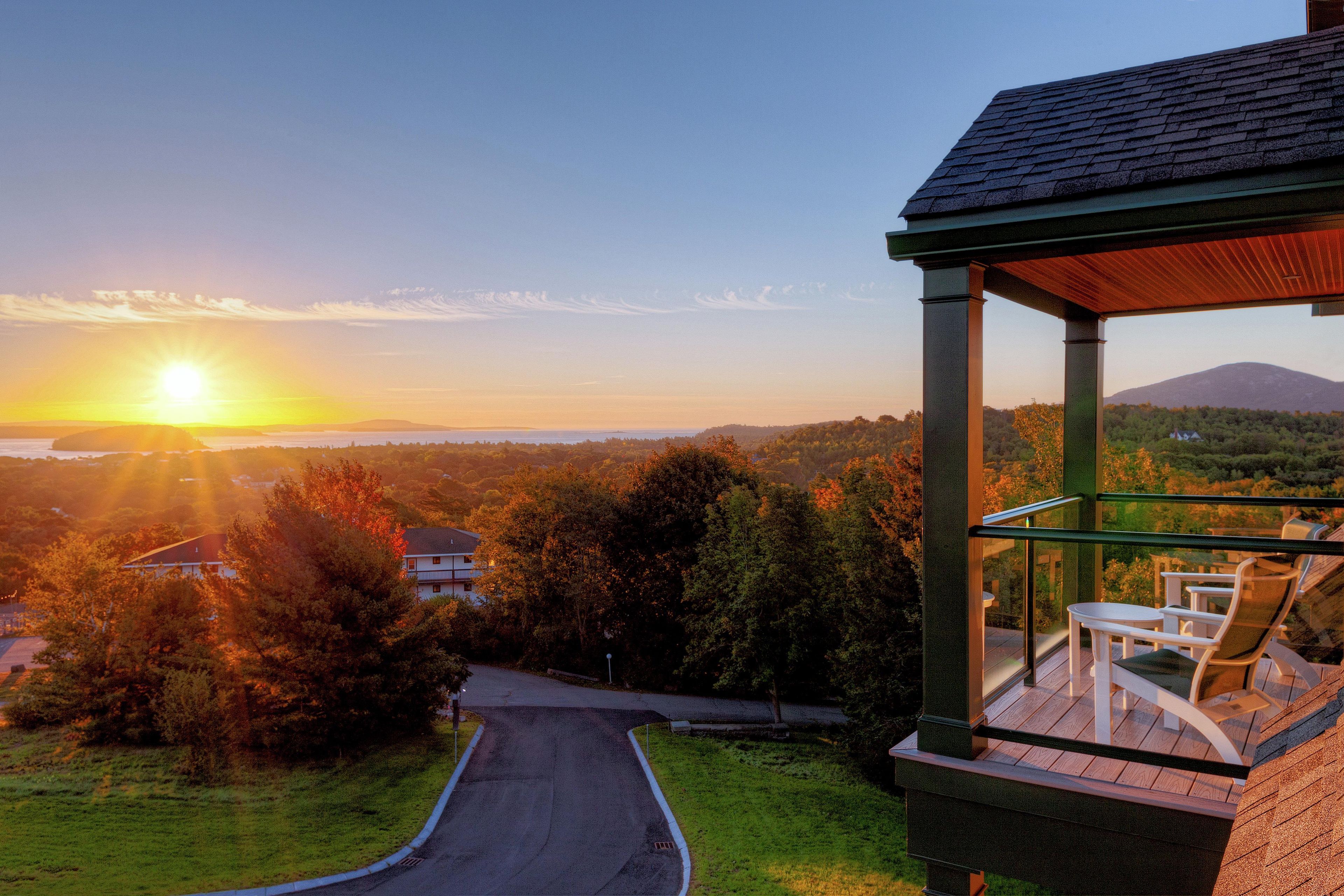 A covered outdoor seating area with a view of a sunset over a hilly landscape.