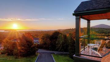 A covered outdoor seating area with a view of a sunset over a hilly landscape.