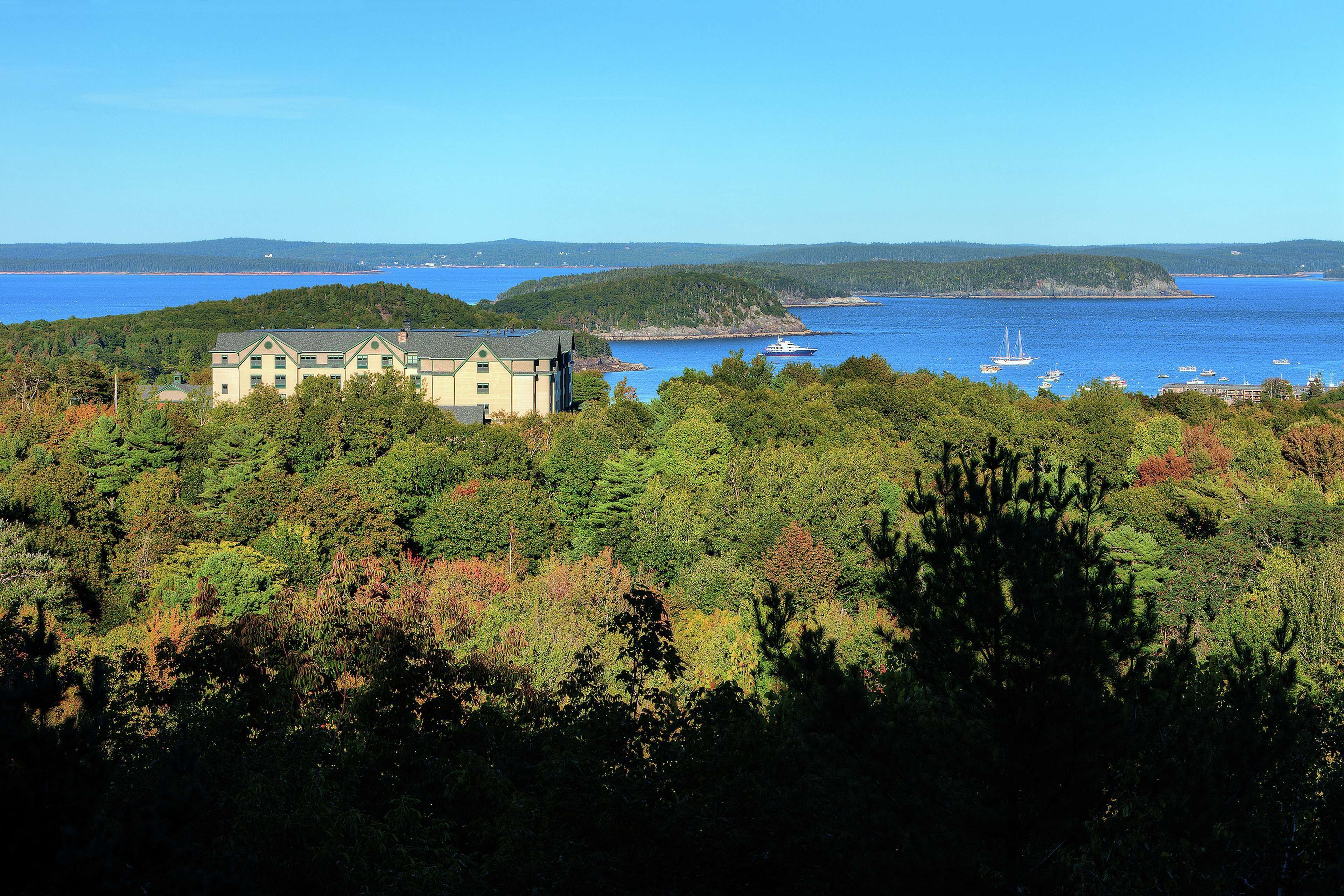 A coastal property with a large building, surrounded by dense forest and a view of the sea.