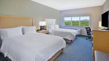 A hotel room with two beds, a desk with a computer, a chair, and a window with a view of greenery.