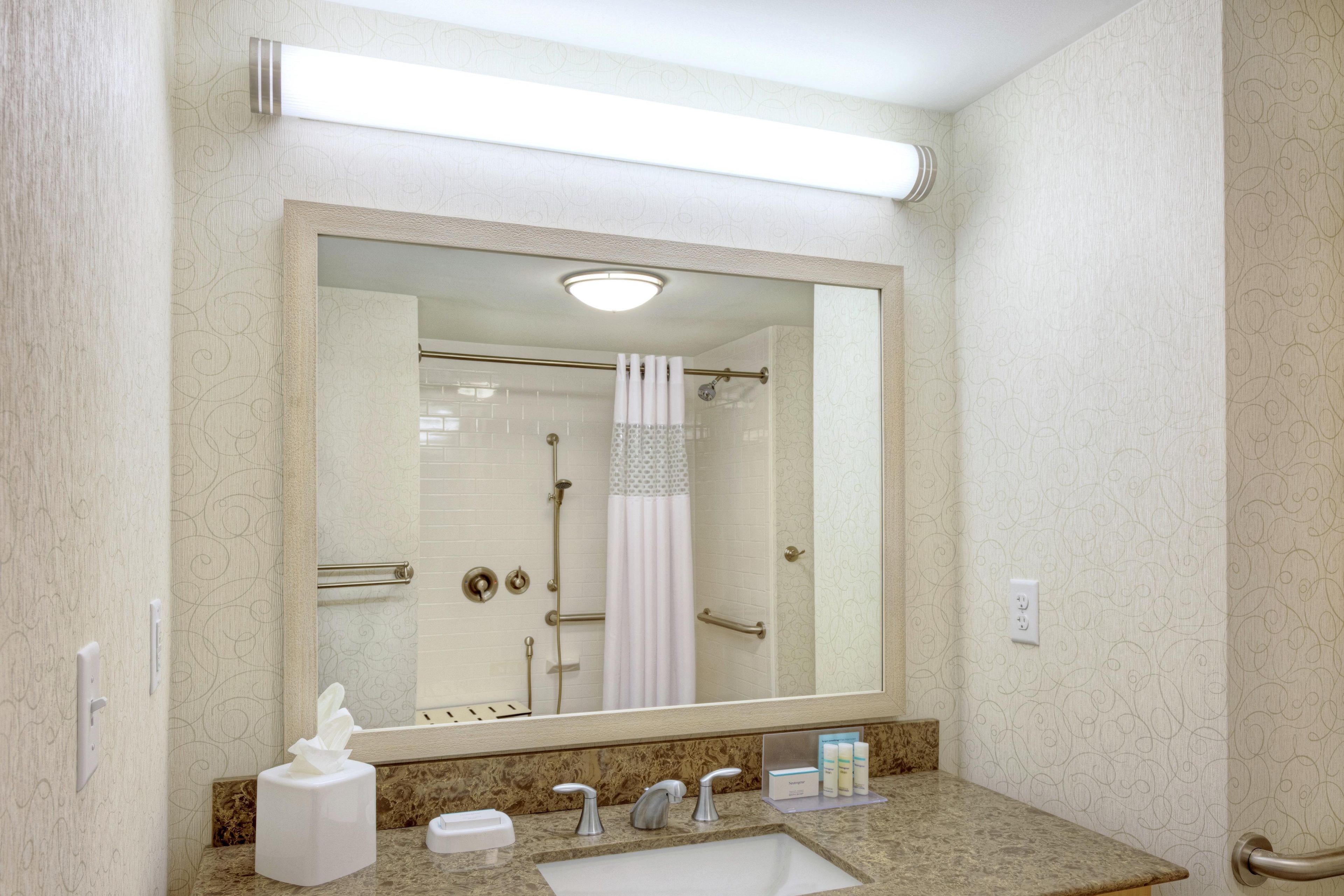 Un baño con un espejo grande, un lavabo, dispensador de toallas y zona de ducha.