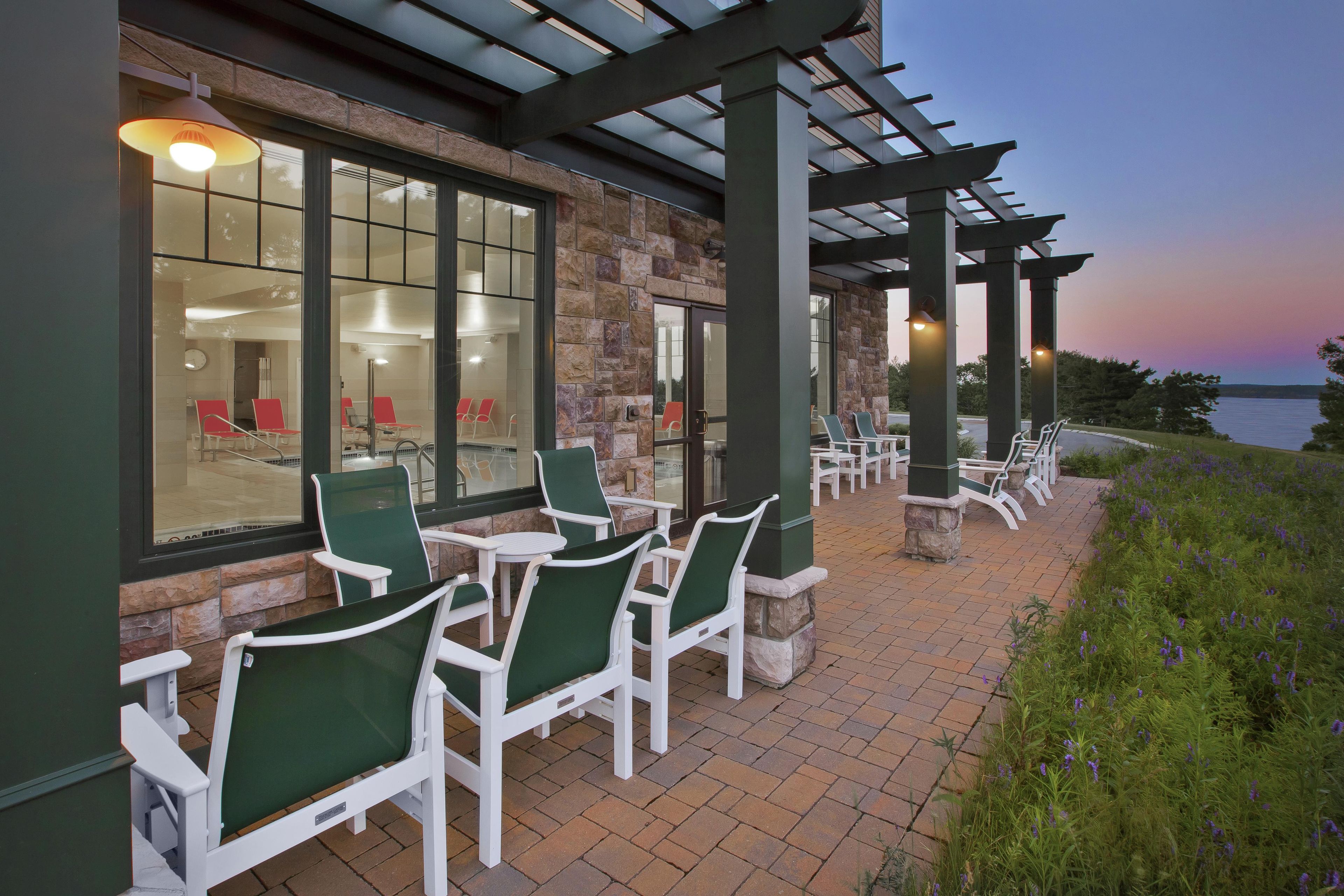 An outdoor patio with white chairs and tables, a stone wall, and a view of the water.