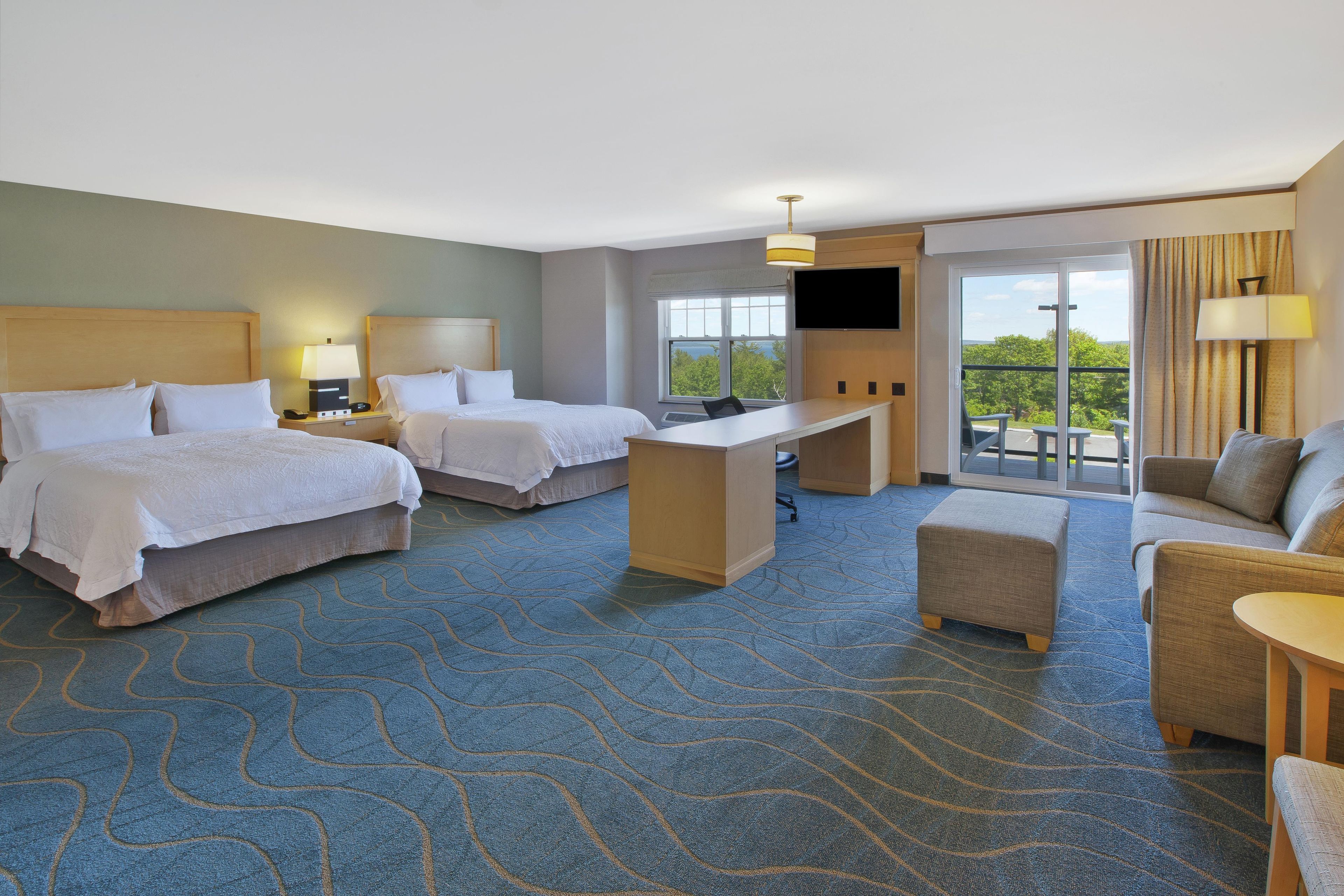 Quarto de hotel com duas camas, uma escrivaninha, um sofá e uma televisão.