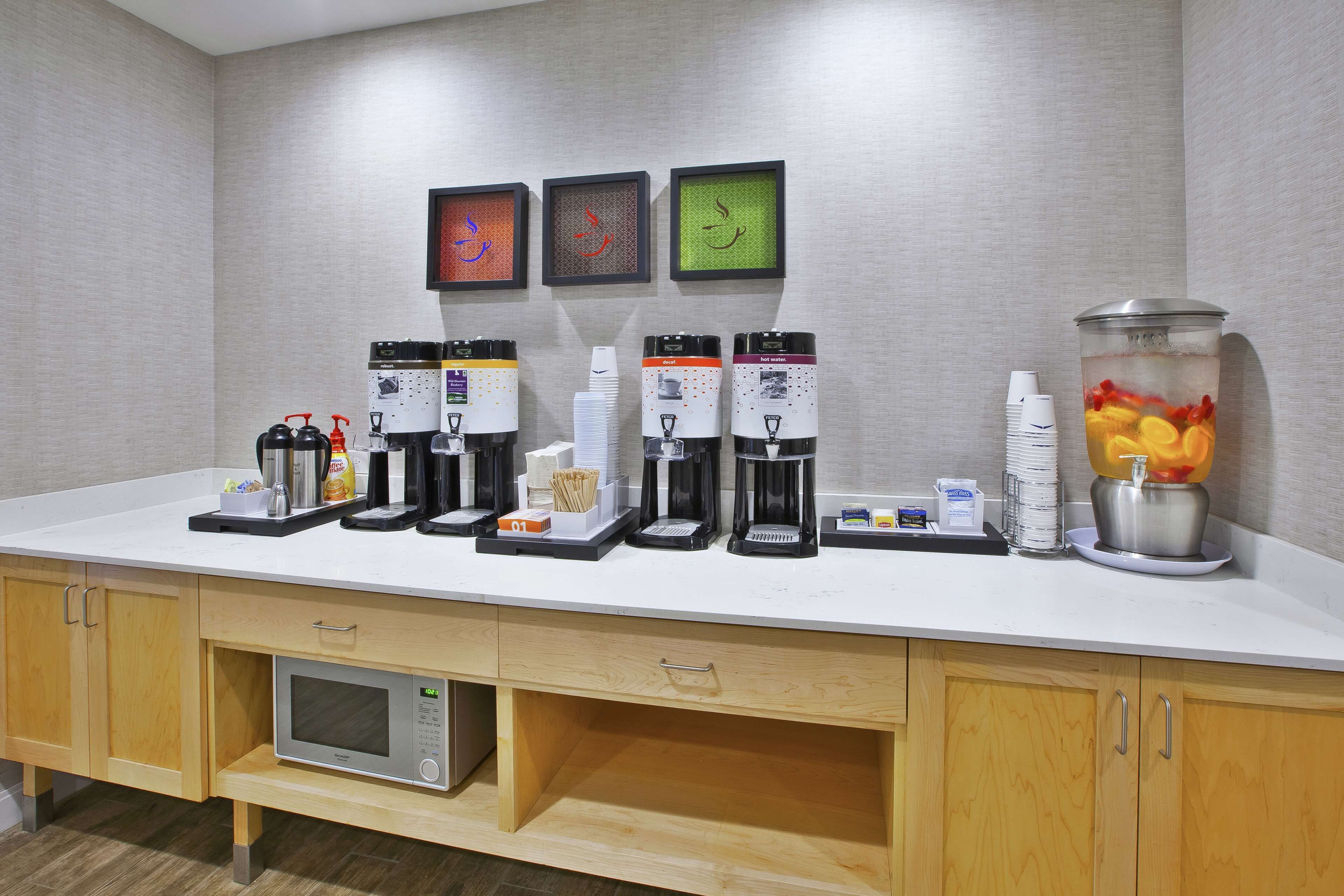 A breakfast bar with multiple coffee makers, a microwave, and a fruit punch dispenser.