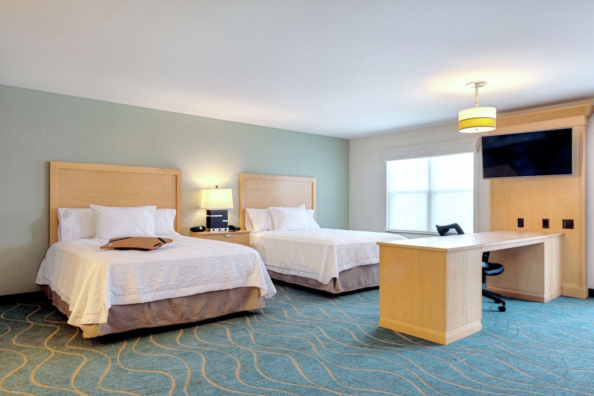 A hotel room with two beds, a desk, and a TV.