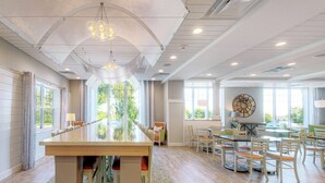 A spacious hotel lobby with a long reception desk, a dining area with multiple tables and chairs, and large windows providing natural light and views of the outdoors. - Hampton by Hilton Bar Harbor (Bar Harbor)