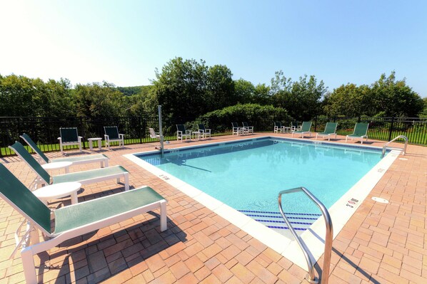 A rectangular swimming pool with a tiled deck, surrounded by green lounge chairs and a metal pool ladder. - Hampton by Hilton Bar Harbor (Bar Harbor)
