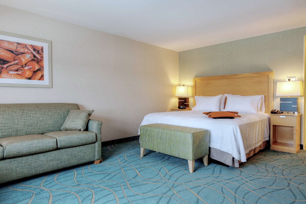 A hotel room with a bed, a sofa, a small table, and a wall-mounted TV.