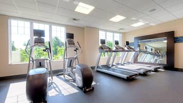 A gym with treadmills, elliptical machines, and a mirror wall.