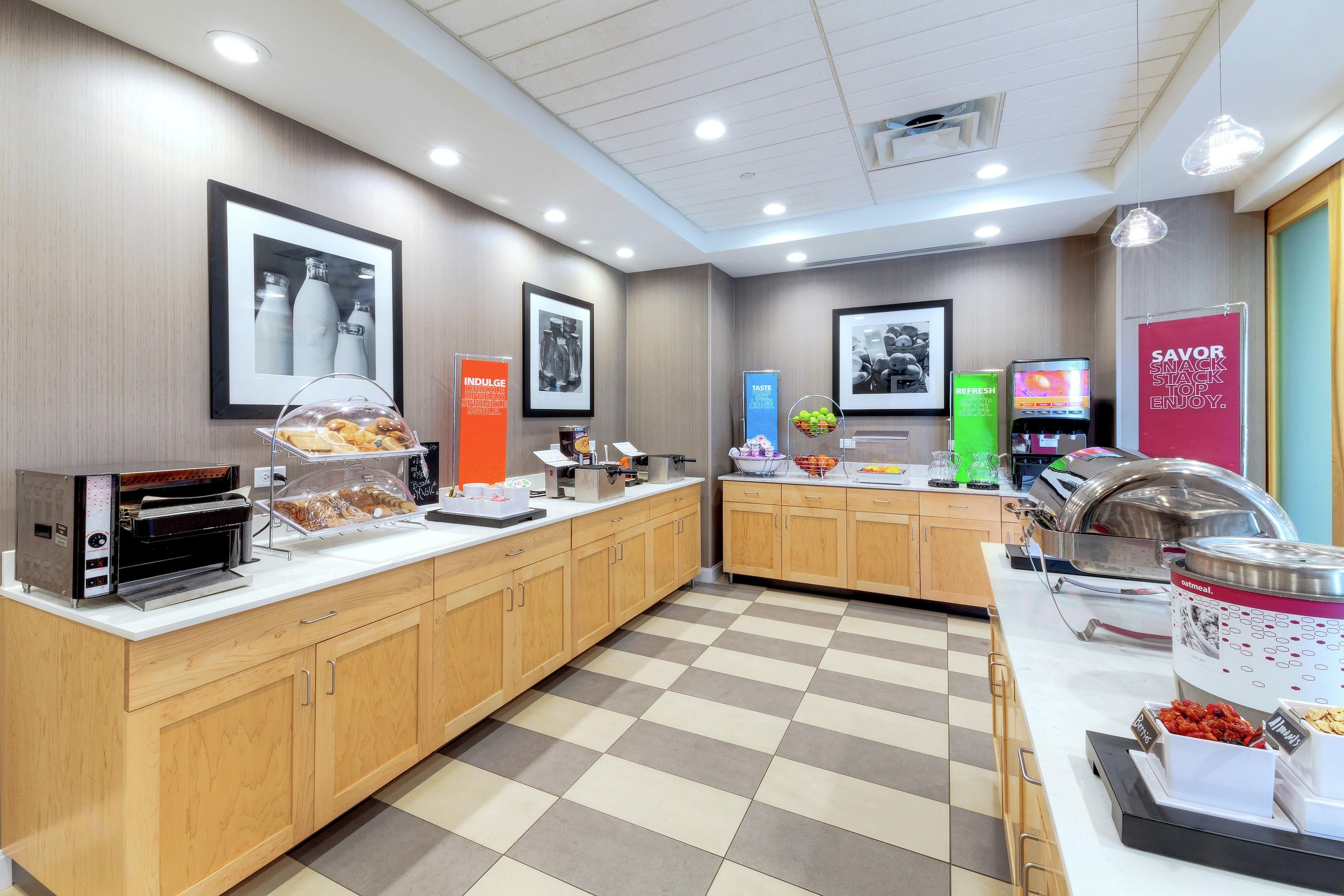 Un espace dédié au petit-déjeuner, équipé d’une machine à café, d’un panier de fruits et d’une pancarte indiquant : « Savourez, dégustez, régalez-vous ! ».
