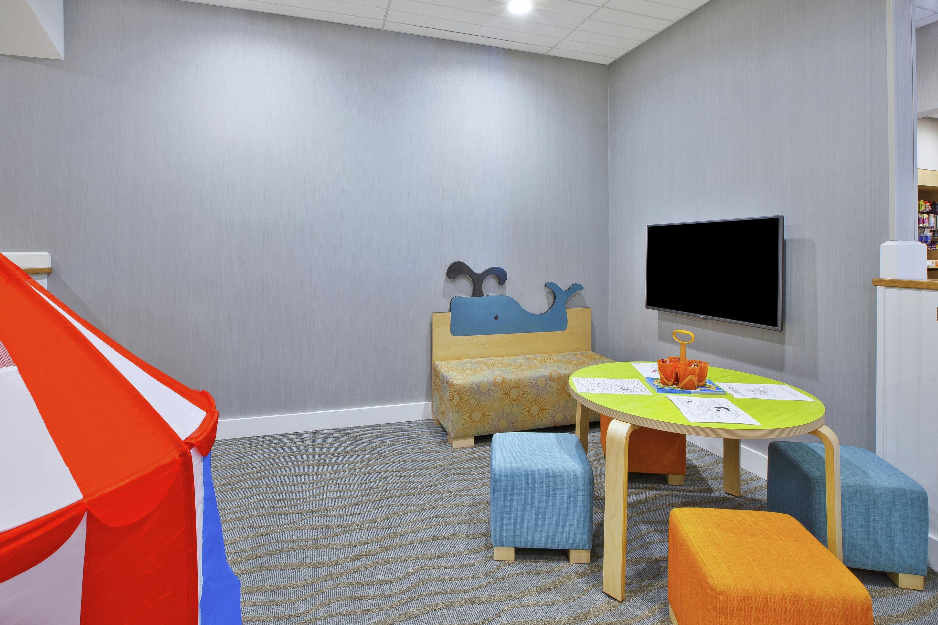 A children's play area with a tent, a sofa, a table with drawings, and a TV.