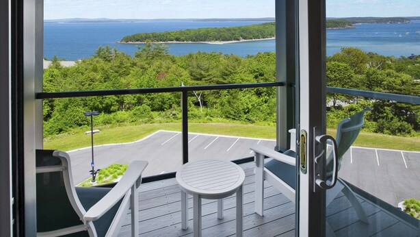 A balcony with a view of the sea, a parking lot, and a small table and chair. - Hampton by Hilton Bar Harbor (Bar Harbor)