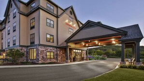 A multi-story hotel with a stone facade, a covered entrance, and a landscaped driveway. - Hampton by Hilton Bar Harbor (Bar Harbor)