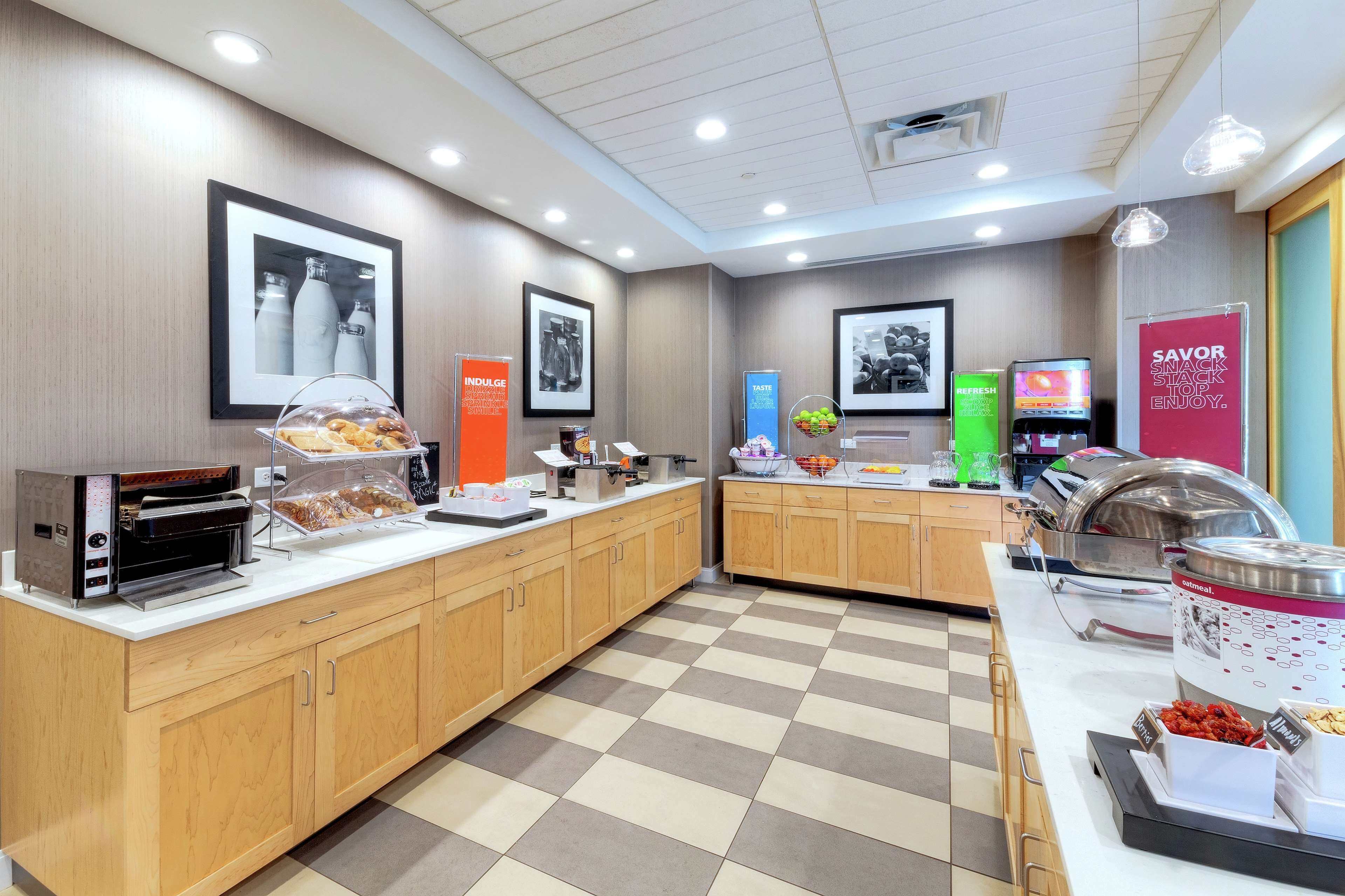 Un espace moderne dédié au petit-déjeuner, équipé d’un buffet où l’on se sert soi-même, d’une machine à café et de différents récipients contenant des aliments.