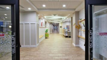A hotel corridor with wooden flooring, a reception desk, a clock, and a sign indicating the flower center.