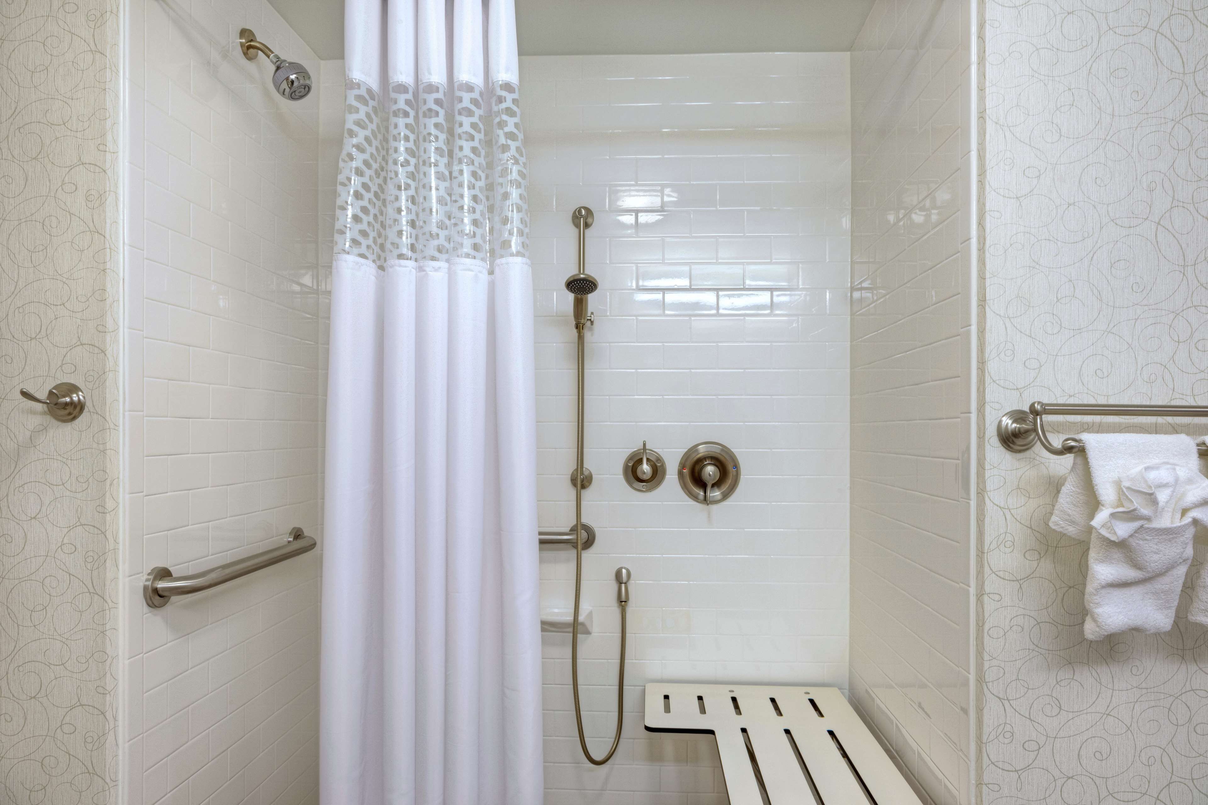 A shower with a white tiled wall, a showerhead, a handheld showerhead, and a towel rack with a towel.