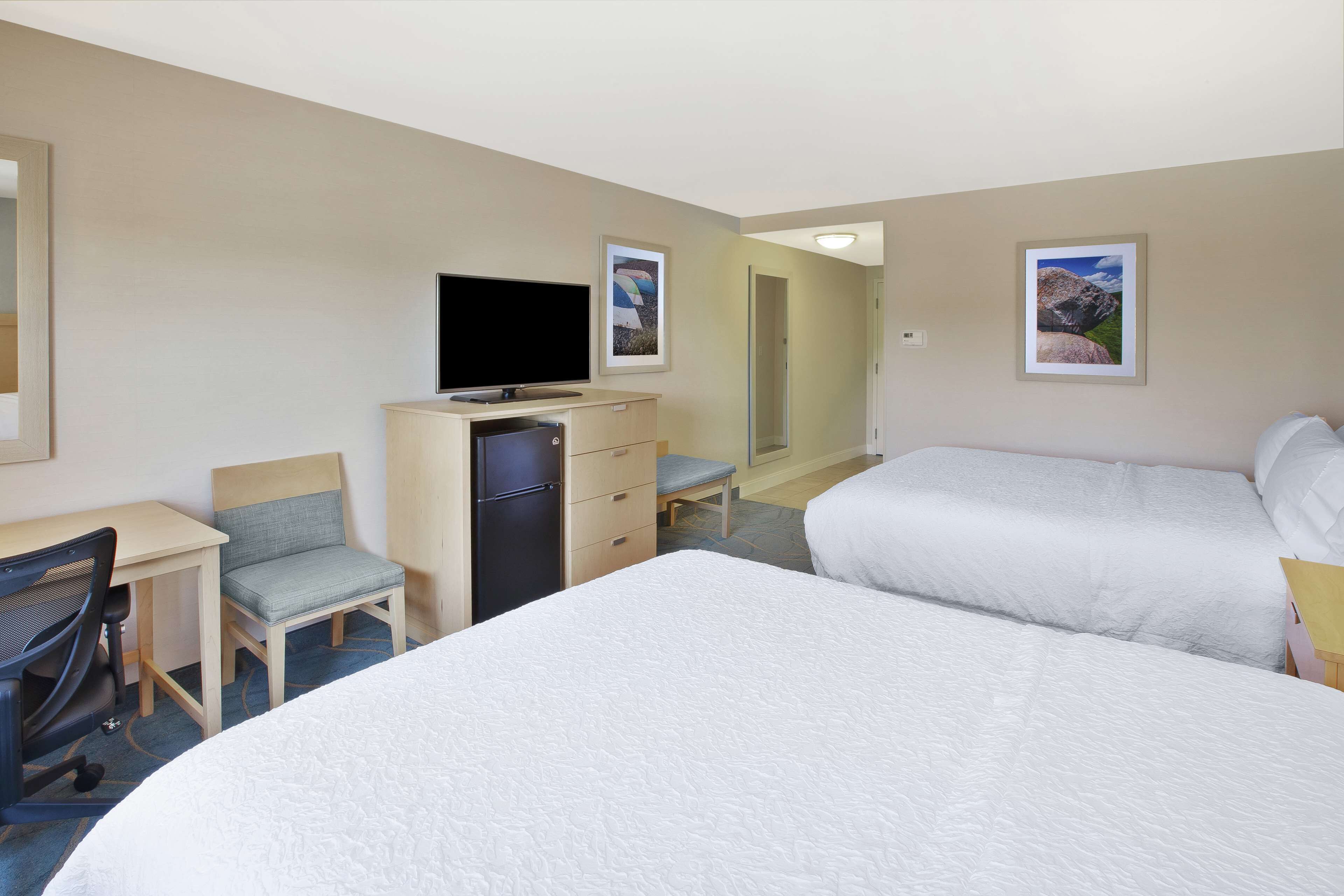 A hotel room with two beds, a desk with a chair, a television, and a small refrigerator.