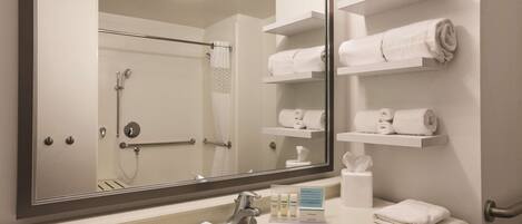 A hotel bathroom with a large mirror, a sink, and shelves with towels.