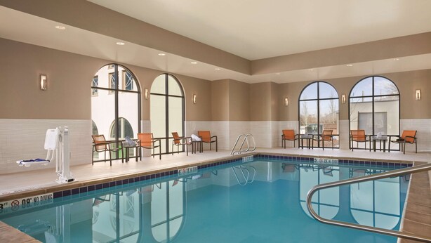 A swimming pool with chairs and sun loungers around it, large arched windows, and a tiled floor. - Hampton Inn Brigham City (Brigham City)