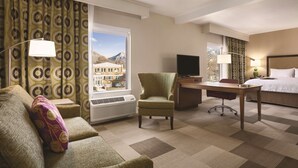 A hotel room with a sofa, armchair, desk, and bed. - Hampton Inn Brigham City (Brigham City)