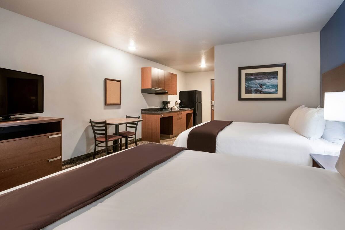 A hotel room with a bed, a desk, a television, a kitchenette, and a painting on the wall.