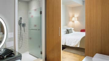 A modern bathroom with a glass shower enclosure, a wooden wardrobe, and a bedside table with a lamp.