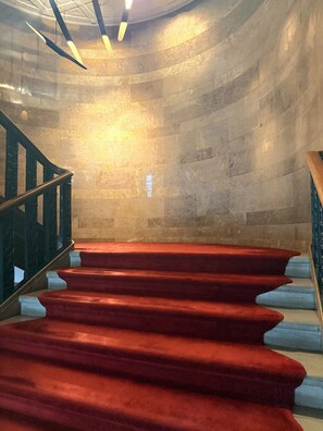 A grand staircase with a red carpet, a curved wall, and a metal railing.