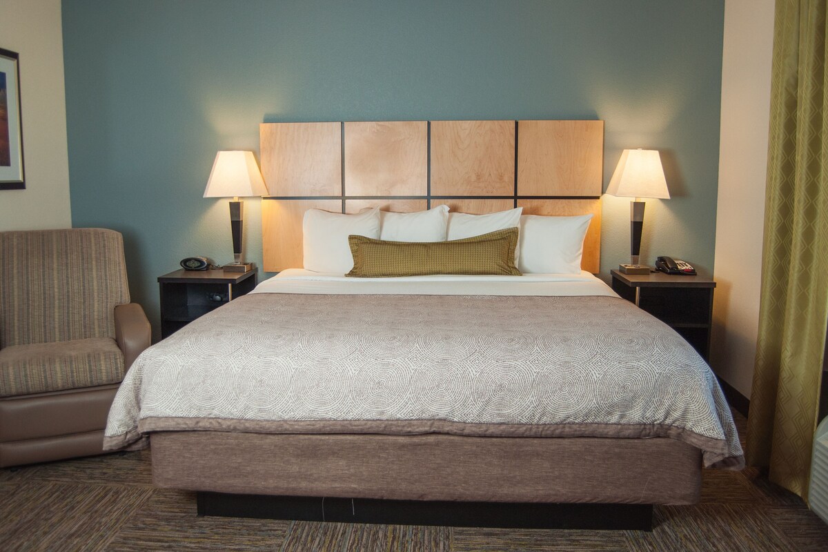 A hotel room with a large bed, two bedside tables with lamps, a chair, and a framed picture on the wall.