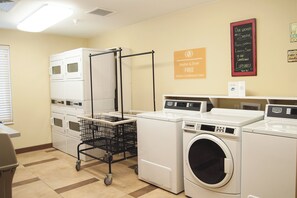 A laundry facility with multiple washing machines and dryers, a cart for laundry items, and signs indicating free laundry soap and detergent. - Candlewood Suites Fort Collins by IHG (Fort Collins)