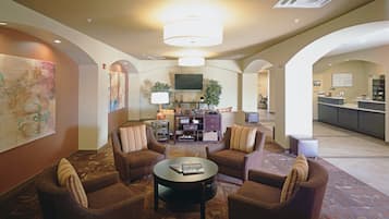 A hotel lobby with a seating area, a flat-screen TV, a reception desk, and a patterned carpet.