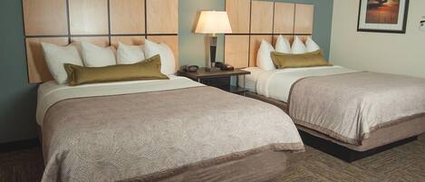 A hotel room with two beds, each with a headboard, a bedside table with a lamp, and a framed picture on the wall.